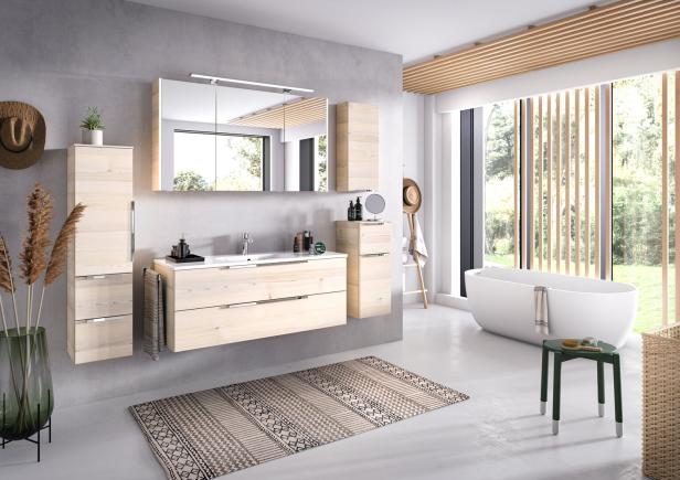 Ein modernes Badezimmer mit hellen Holzmöbeln, einer Badewanne und einem gemusterten Teppich.