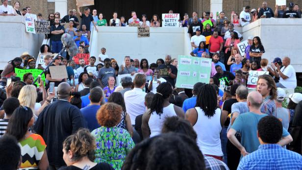 Eine Menschenmenge demonstriert mit Schildern, auf denen „Arrest Betty Shelby“ und „Gerechtigkeit für alle“ steht.