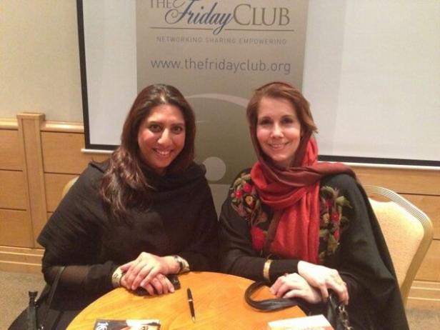 Zwei Frauen sitzen an einem Tisch vor einem Banner des „The Friday Club“.