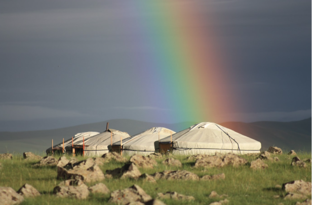 Ein Regenbogen erstreckt sich über eine Gruppe von Jurten in einer hügeligen Landschaft.
