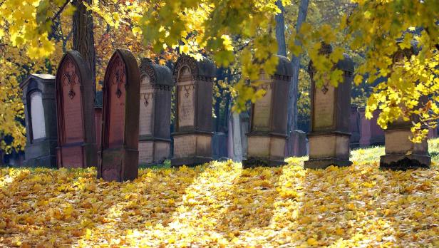 Herbstliche Stimmung auf einem Friedhof mit gelben Blättern und alten Grabsteinen.