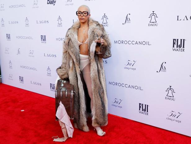 Doja Cat mit Pelzmantel und Koffer auf einem roten Teppich.