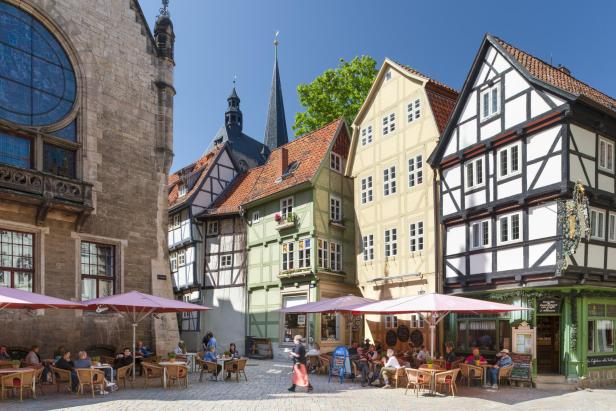 Belebter Marktplatz in mittelalterlicher Stadt mit Fachwerkhäusern und Cafés.