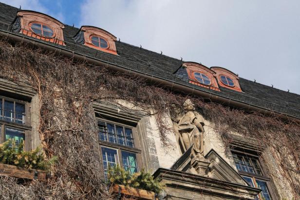 Eine Steinfigur schmückt die Fassade eines alten Hauses, das von Kletterpflanzen bewachsen ist.