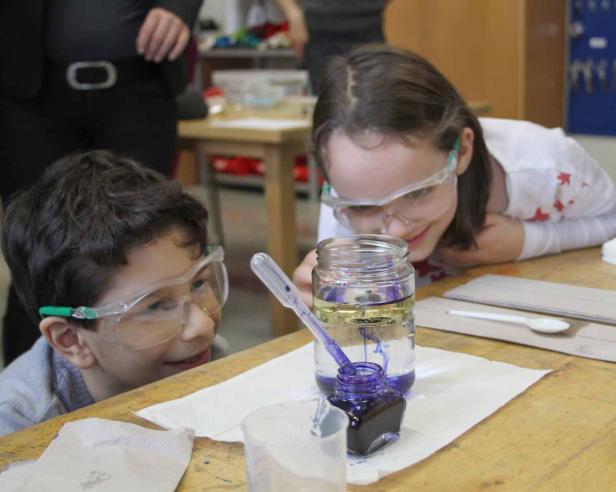 Zwei Kinder mit Schutzbrillen beobachten ein Experiment mit Öl, Wasser und Tinte.