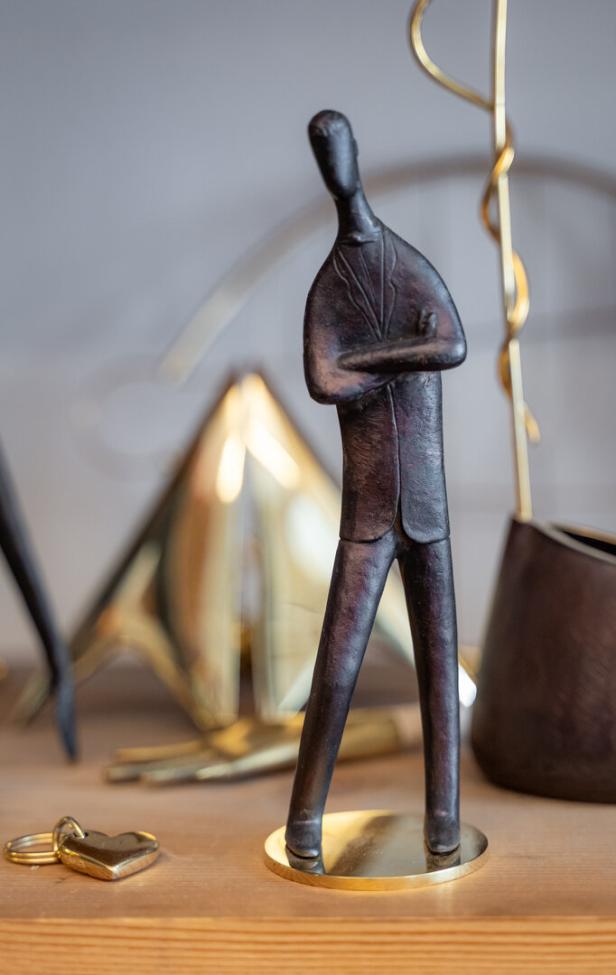 Eine patinierte Messingfigur zeigt einen Mann mit verschränkten Armen.