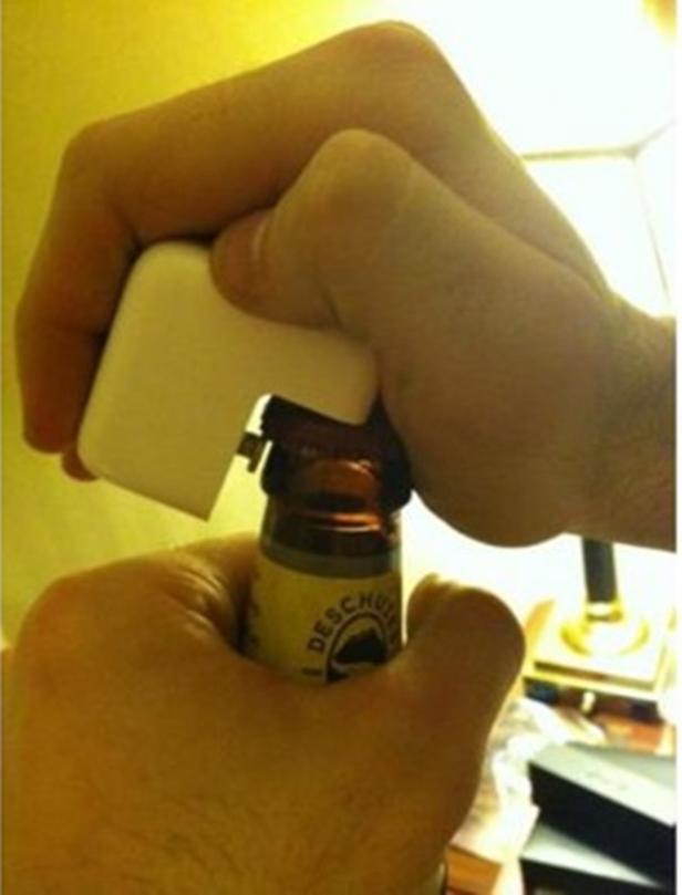 Eine Person öffnet eine Bierflasche mit einem weißen, ungewöhnlichen Flaschenöffner.