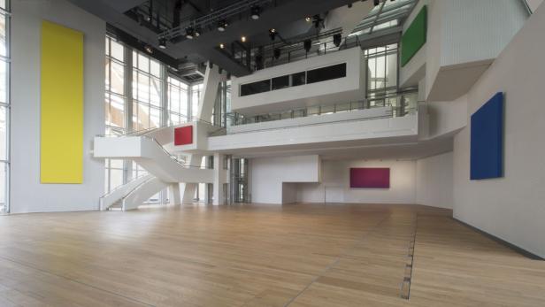 Ein großer, leerer Raum mit farbigen Wandbildern und einer weißen Treppe.