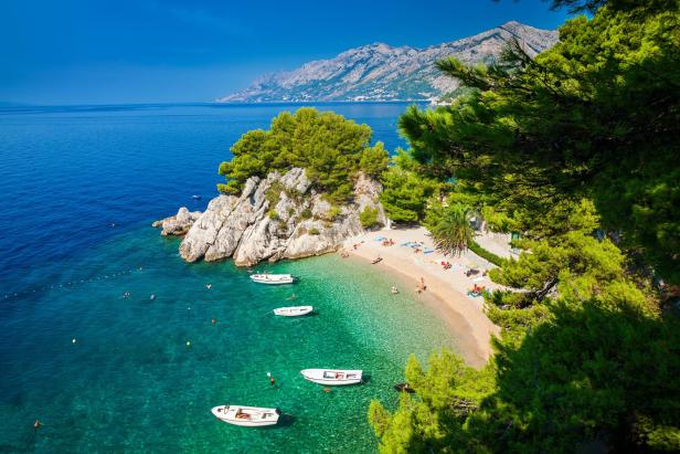 Ein malerischer Strand mit klarem Wasser, Booten und Menschen in Brela, Kroatien.
