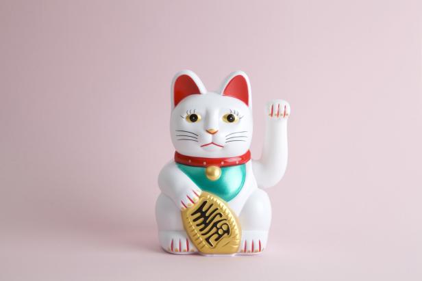 Eine weiße asiatische Winkekatze hebt ihre linke Tatze zum Winken: Maneki-neko lockt Geld, Glück oder Kundschaft an.