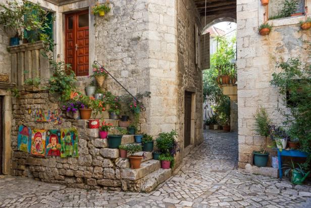 Eine malerische Gasse mit Steintreppen, Blumentöpfen und Kunstwerken in einer Altstadt.