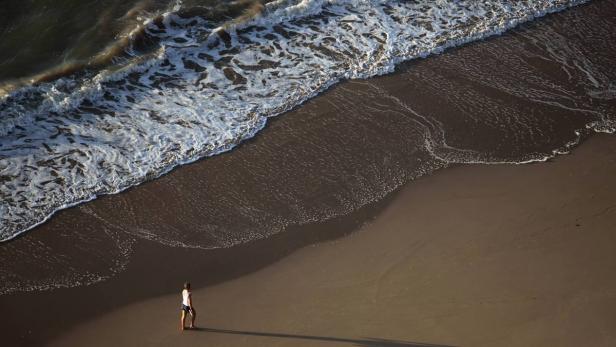 Eine Frau geht am Strand entlang, während die Wellen an den Ufern brechen.