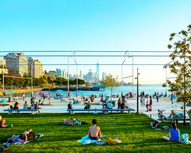 Menschen entspannen sich an einem sonnigen Tag am Strand mit Blick auf die Skyline von New York City.