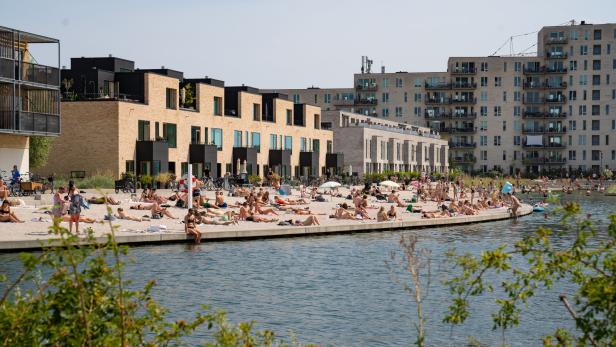 Viele Menschen sonnen sich an einem Strand in der Nähe von modernen Wohngebäuden.
