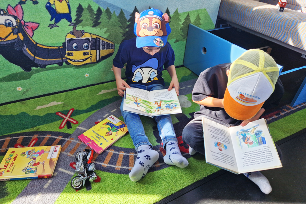 Zwei Kinder sitzen auf einem Teppich und lesen Bücher.
