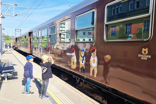 Zwei Kinder stehen an einem Bahnsteig vor einem Zug der „Ötscher-Bar“.