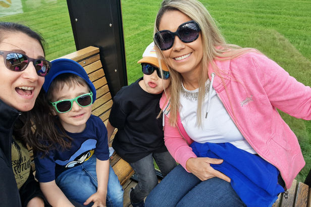 Eine Frau macht mit zwei Kindern und einer weiteren Frau ein Selfie auf einer Bank im Freien.