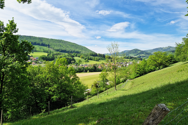Blick über grüne Hügel auf ein Dorf unter blauem Himmel.