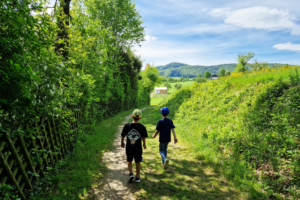 Zwei Jungen gehen einen grünen Pfad entlang in Richtung einer ländlichen Szene.