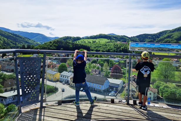 Zwei Kinder genießen die Aussicht von einem Aussichtsturm auf eine grüne Landschaft.