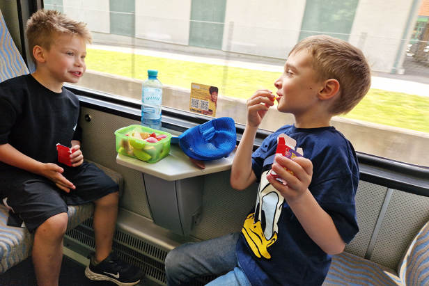 Zwei Jungen sitzen im Zug und essen Süßigkeiten und Obst.