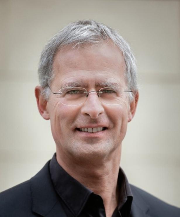 Ein Mann mit grauen Haaren und Brille lächelt in die Kamera.
