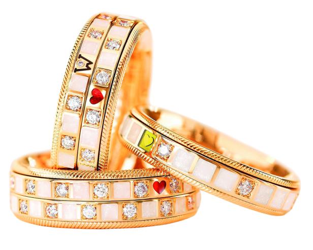 Drei goldene Ringe mit Diamanten, Herzen und dem Buchstaben „M“ liegen übereinander.