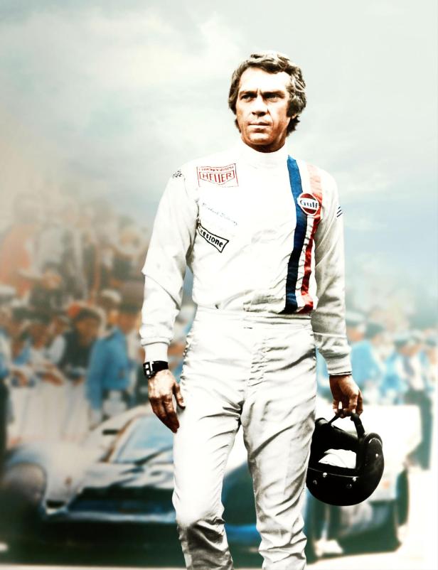 Steve McQueen in Rennfahrerkluft mit Helm in der Hand.