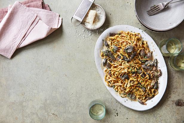 Teller mit Tagliatelle in Morcheln mit Sauce, daneben Geschirr und Parmesan mit Reibe, Rezeptfoto