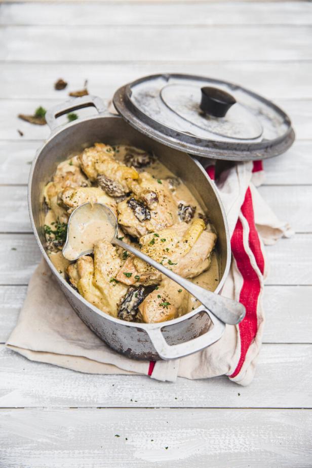 Huhn mit Morcheln und Sahnesauce in einem Bräter serviert, mit Schöpflöffel und einem Geschirrtuch