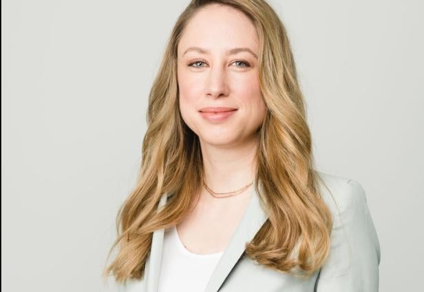 Eine Frau mit blonden, gewellten Haaren und einem hellblauen Blazer lächelt. Eine Frau mit blonden, gewellten Haaren und einem hellblauen Blazer lächelt.