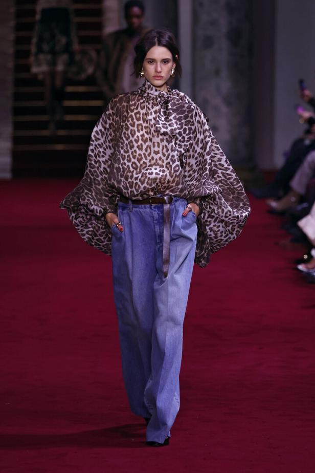Eine Frau in einer Leopardenbluse und Jeans auf einem roten Laufsteg.