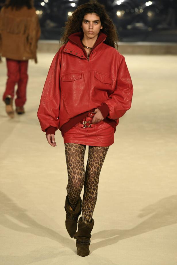 Eine Frau auf dem Laufsteg trägt eine rote Lederjacke, einen Minirock und Leggings mit Leopardenmuster.