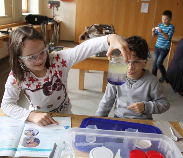 Zwei Kinder experimentieren mit Schutzbrillen und einem Glas mit Flüssigkeiten im Unterricht.