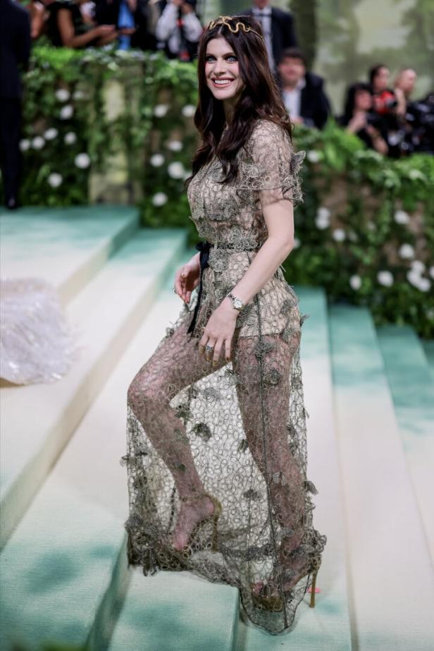 Alexandra Daddario auf einer Treppe in einem transparenten, verzierten Kleid.