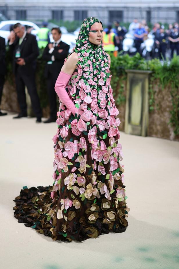 Eine Person in einem langen Kleid, das mit Rosen und Blättern bedeckt ist, mit passender Kopfbedeckung.