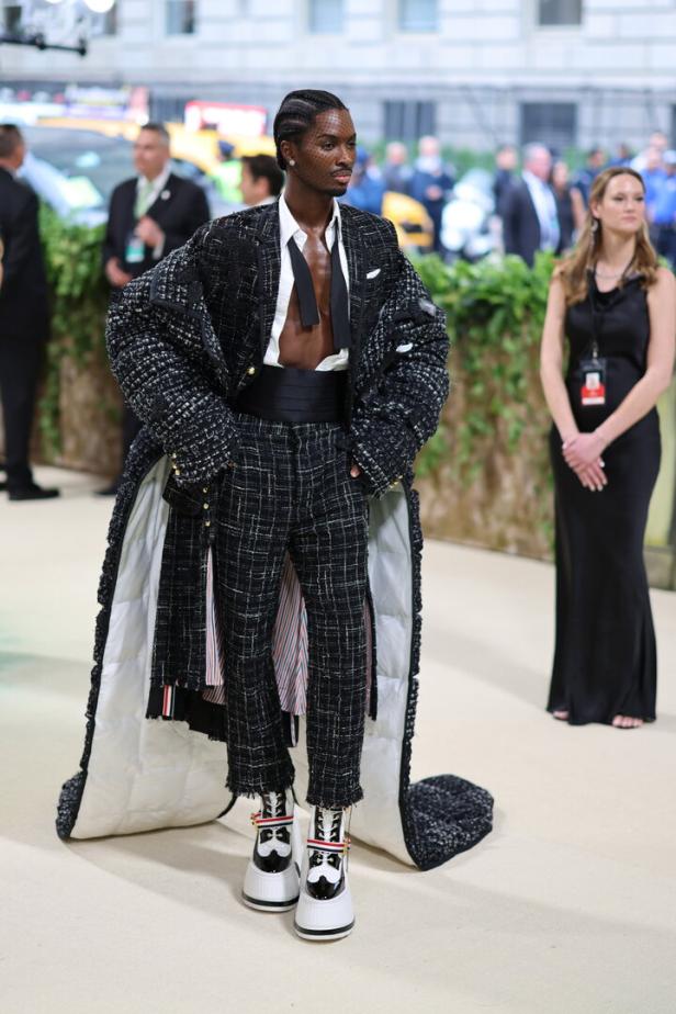 Ein Mann in einem extravaganten Tweed-Anzug mit Plateauschuhen posiert auf einem Teppich.