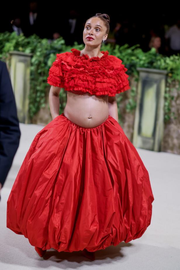 Eine schwangere Frau in einem roten, extravaganten Kleid auf dem Laufsteg.