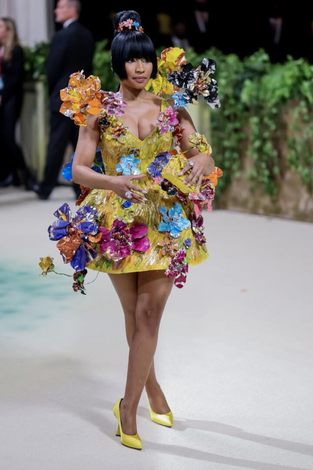 Eine Frau in einem gelben Kleid mit bunten Blumenapplikationen und passenden Schuhen.