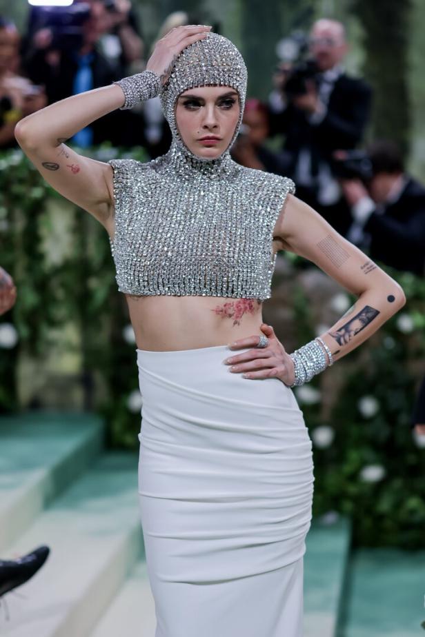 Cara Delevingne trägt ein silbernes, mit Strass besetztes Top und einen passenden Kopfschmuck.