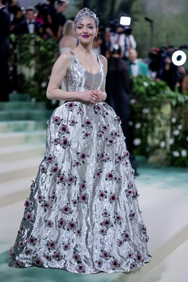 Amanda Seyfried in einem silbernen Kleid mit Blumenapplikationen und einer Tiara.