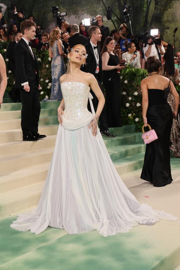 Ariana Grande in einem weißen Kleid auf dem grünen Teppich.