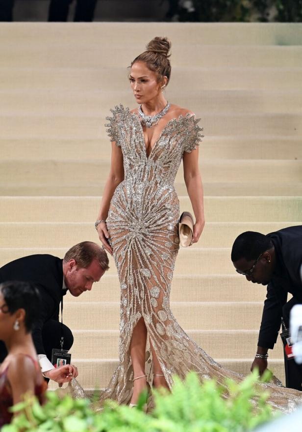 Jennifer Lopez in einem silbernen, bodenlangen Kleid auf einer Treppe.