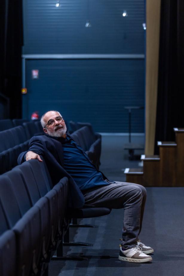 Ein Mann mit Bart sitzt entspannt in einem leeren Theatersaal.