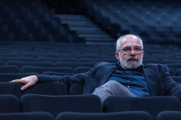 Ein Mann mit Brille und Bart sitzt in einem leeren Theatersaal.