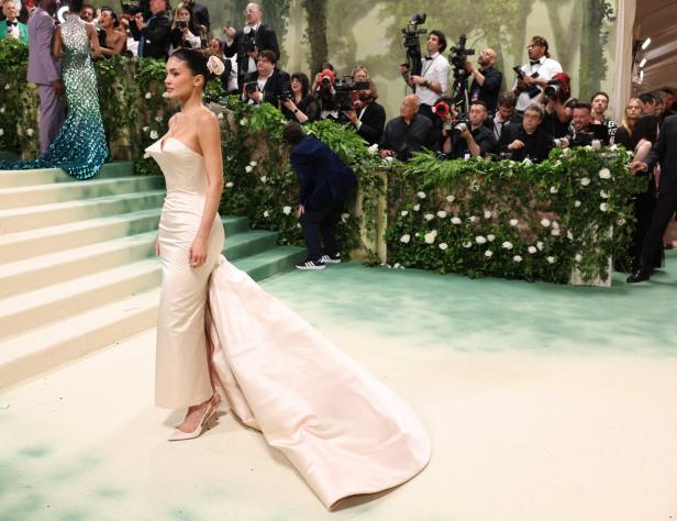 Kylie Jenner in einem elfenbeinfarbenen Kleid auf dem roten Teppich, umgeben von Fotografen.
