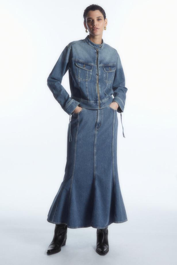 Eine Frau in einem Jeansensemble aus Jacke und Maxirock mit Stiefeln.