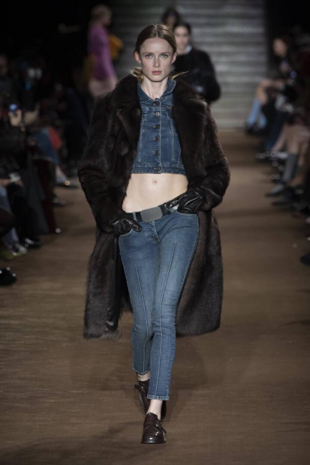 Eine Frau in Jeans, Jeansjacke und einem braunen Pelzmantel auf einem Laufsteg.