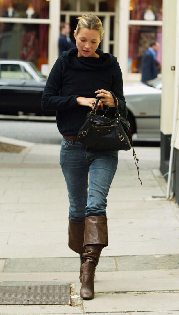 Kate Moss geht mit Jeans, Stiefeln und Handtasche die Straße entlang.