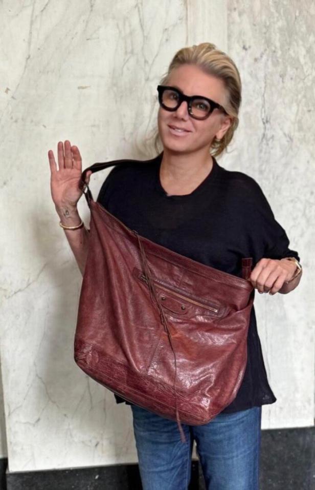 Eine Frau mit Brille präsentiert eine große, rote Ledertasche.